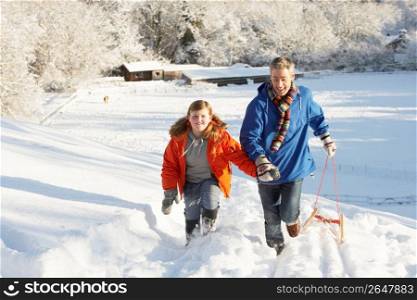 Father And Son Pulling Sledge Up Snowy Hill