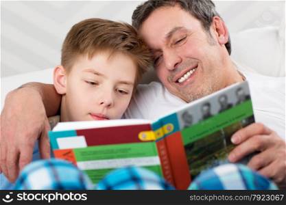 Father and son reading a book. Careful dad helping child to learn new things. Son and father reading book together