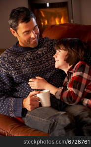 Father And Son Relaxing With Hot Drink By Cosy Log Fire