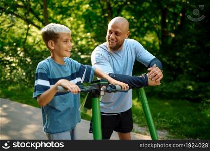 Father and son riding on kick scooters on walking path outdoors. The family leads a healthy lifestyle, sport workout in summer park. Father and son riding on kick scooters in park