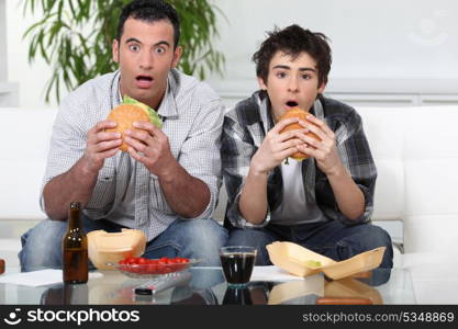 Father and son sat on the sofa eating burgers