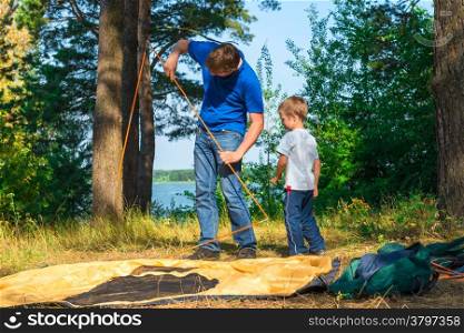 father and son set the tent on the lake