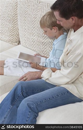 Father and son sit reading a digital book