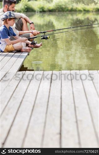 Father and son sitting on pier while fishing in lake