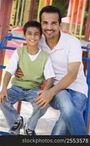Father and son sitting on playground structure smiling (selective focus)