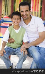 Father and son sitting on playground structure smiling (selective focus)