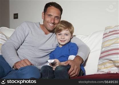 Father And Son Sitting On Sofa Watching TV Together