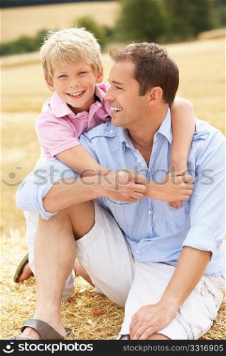 Father And Son Sitting On Straw Bales In Harvested Field