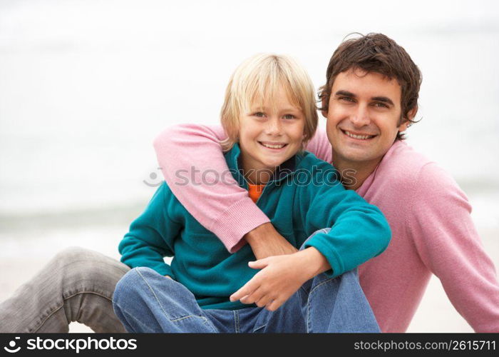 Father And Son Sitting On Winter Beach Together