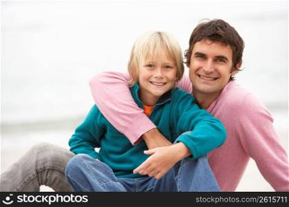 Father And Son Sitting On Winter Beach Together