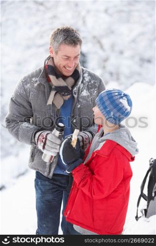 Father And Son Stopping For Hot Drink And Snack On Walk Through Snowy Landscape