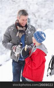 Father And Son Stopping For Hot Drink And Snack On Walk Through Snowy Landscape