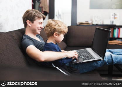 Father and son using laptop on sofa in house