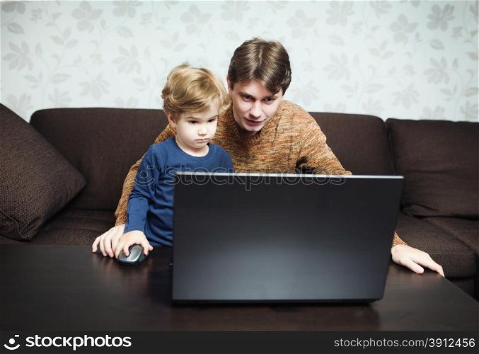 Father and son using laptop on sofa in house