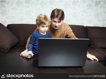 Father and son using laptop on sofa in house