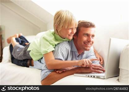 Father And Son Using Laptop Relaxing Sitting On Sofa At Home