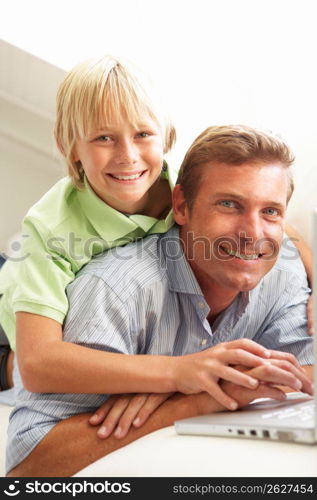 Father And Son Using Laptop Relaxing Sitting On Sofa At Home