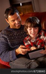 Father And Son Using Tablet Computer By Cosy Log Fire