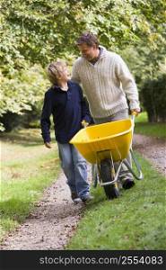 Father and son walking on path pushing wheelbarrow