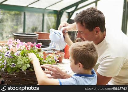 Father And Son Watering Plants In Greenhouse