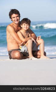 Father And Son Wearing Swimwear Sitting On Sandy Beach