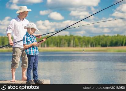 father and son with fishing rods on a wooden pier near the lake on a sunny day