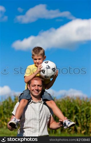 Father and son with football; he is carrying the son on the shoulders
