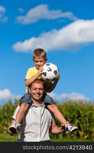 Father and son with football; he is carrying the son on the shoulders