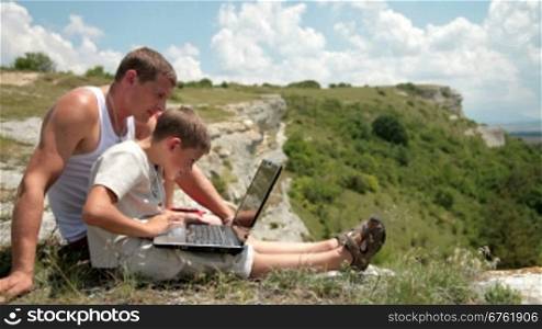 Father and son with laptop in the mountains