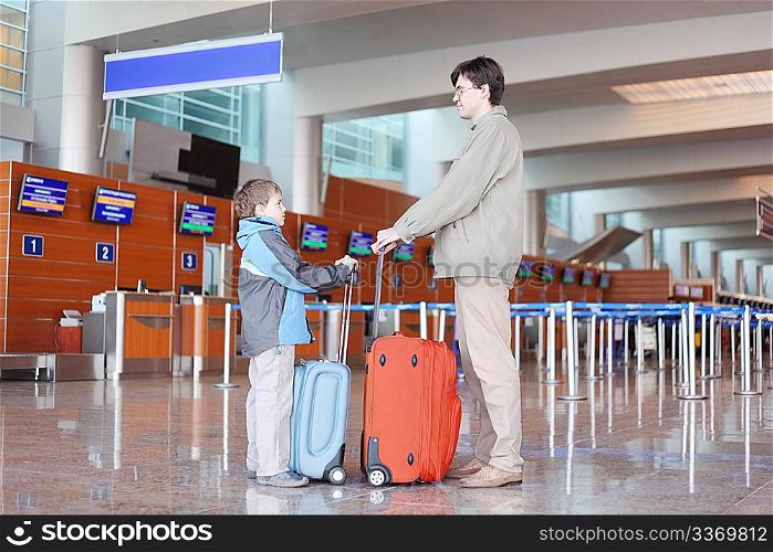 father and son with red suitcase standing in airport hall side view