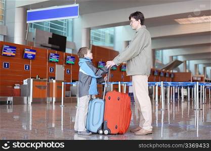 father and son with suitcases standing in airport hall side view
