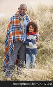 Father And Son Wrapped In Blanket Amongst Dunes On Winter Beach