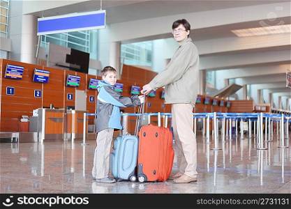 father and sonl with red suitcase standing in airport hall side view looking at camera