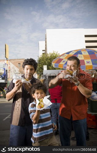 Father and sons eat hot dogs from street vendor