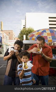 Father and sons eat hot dogs from street vendor