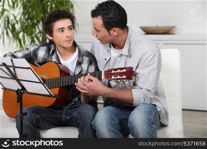 father and teenage son playing the guitar