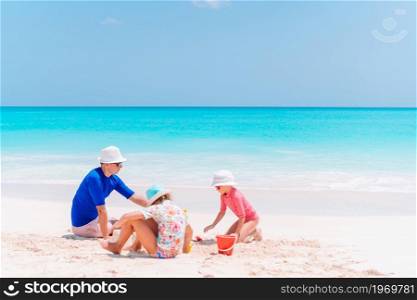 Father and two girls playing with sand on tropical beach. Family playing with beach toys. Father and kids making sand castle at tropical beach. Family playing with beach toys