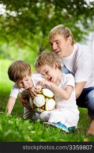 Father and two sons play football in a summer garden