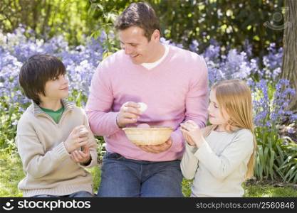 Father and two young children on Easter looking for eggs outdoors smiling