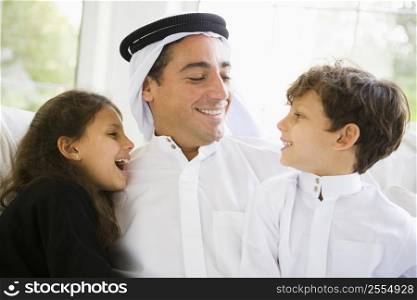 Father and two young children sitting in living room smiling (high key/selective focus)