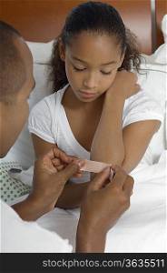 Father applying bandaid to daughter (7-9) in bed