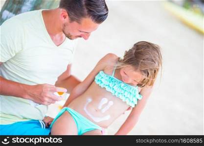 Father applying sun cream to daughter body. Young father applying sun cream to daughter on the beach. Sun protection