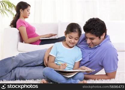 Father assisting child in drawing with woman sitting in the background