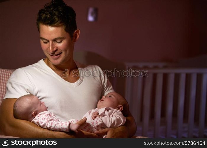 Father At Home Cuddling Twin Baby Daughters In Nursery