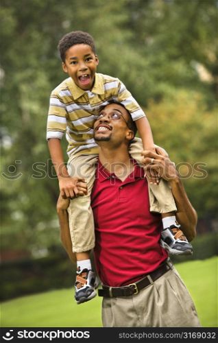 Father carrying his son on his shoulders smiling and looking at eachother.