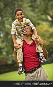 Father carrying his son on his shoulders smiling and looking at eachother.