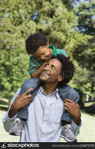 Father carrying son on shoulders in park.