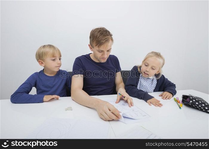 Father checking children&rsquo;s homework at table