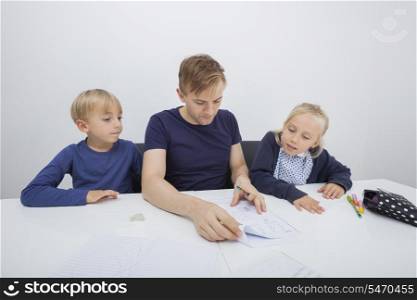 Father checking children&rsquo;s homework at table