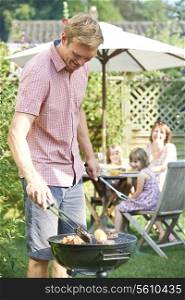 Father Cooking Barbeque For Family In Garden At Home